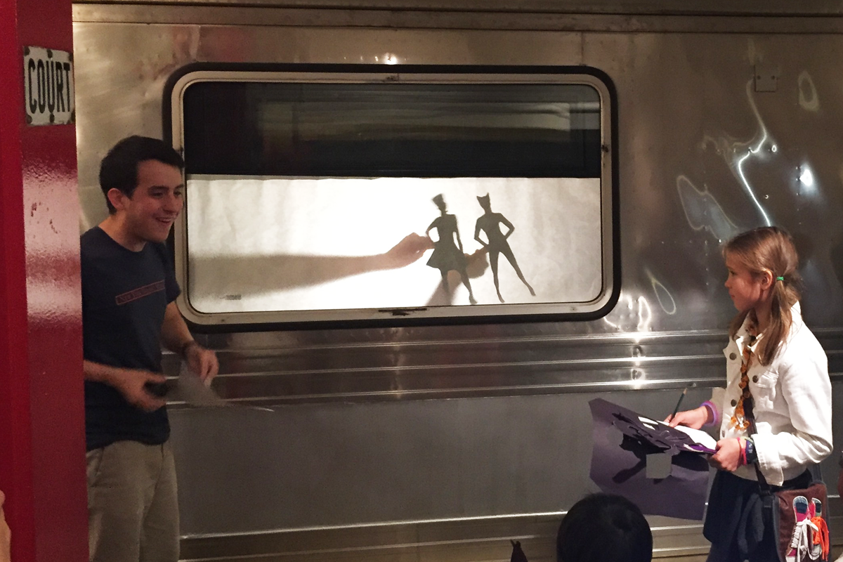 An educator and young transit fan create shadow puppets in the subway.