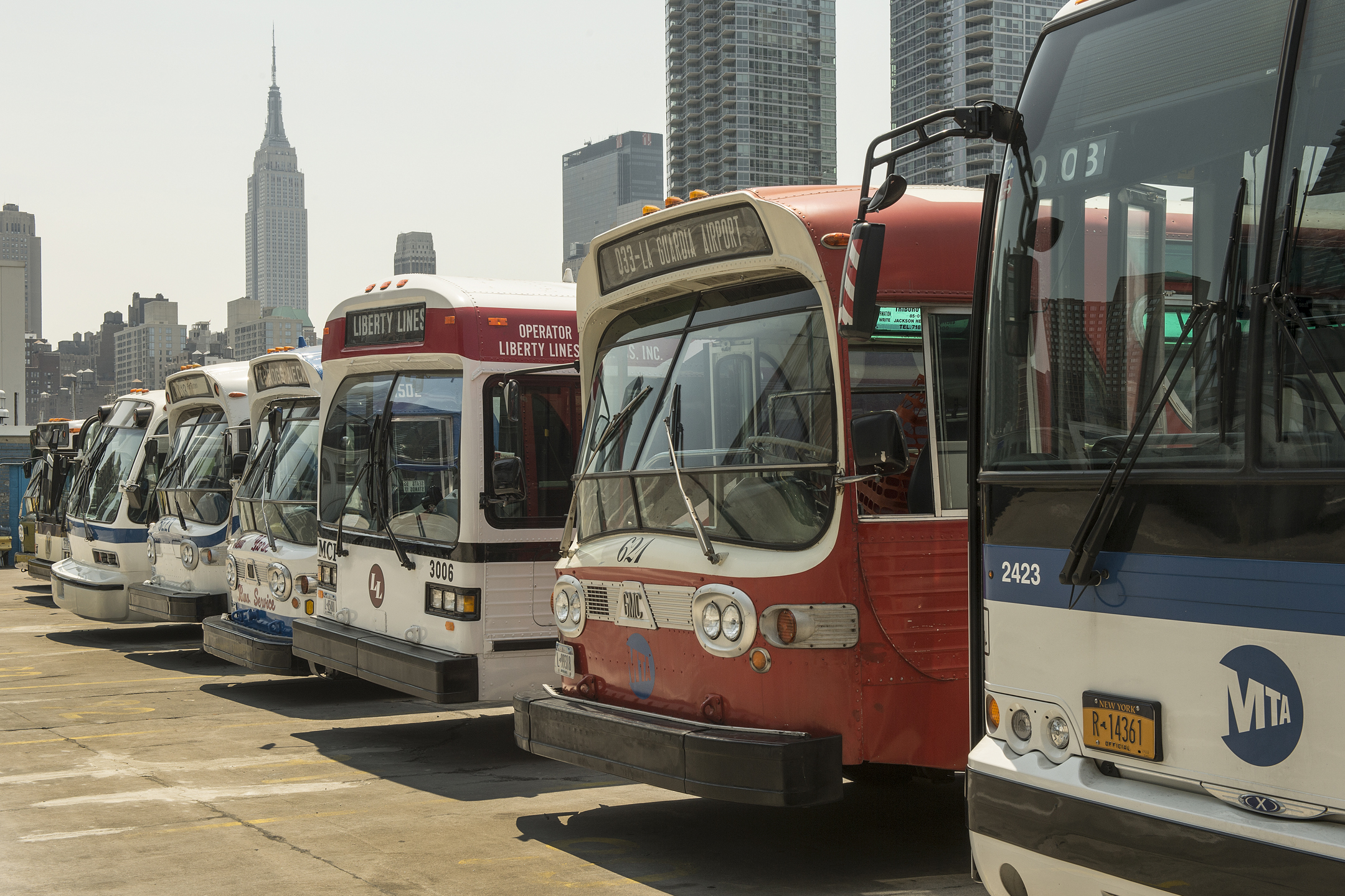 5 vintage buses lined up in a parking lot in front of skyscrapers