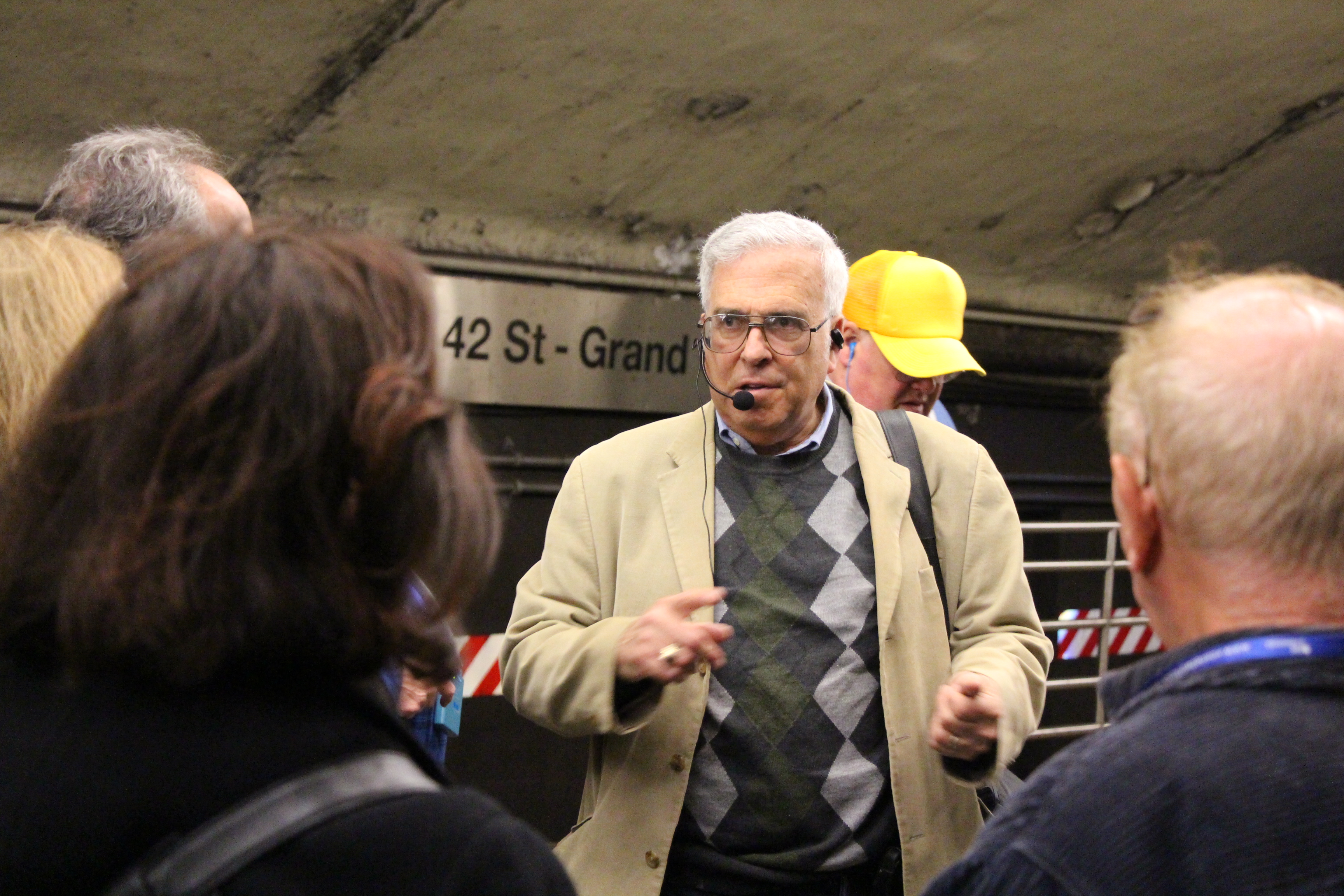 Andrew Sparberg speaks into a microphone in front of a tour group on the 7 platform at Grand Central Terminal.