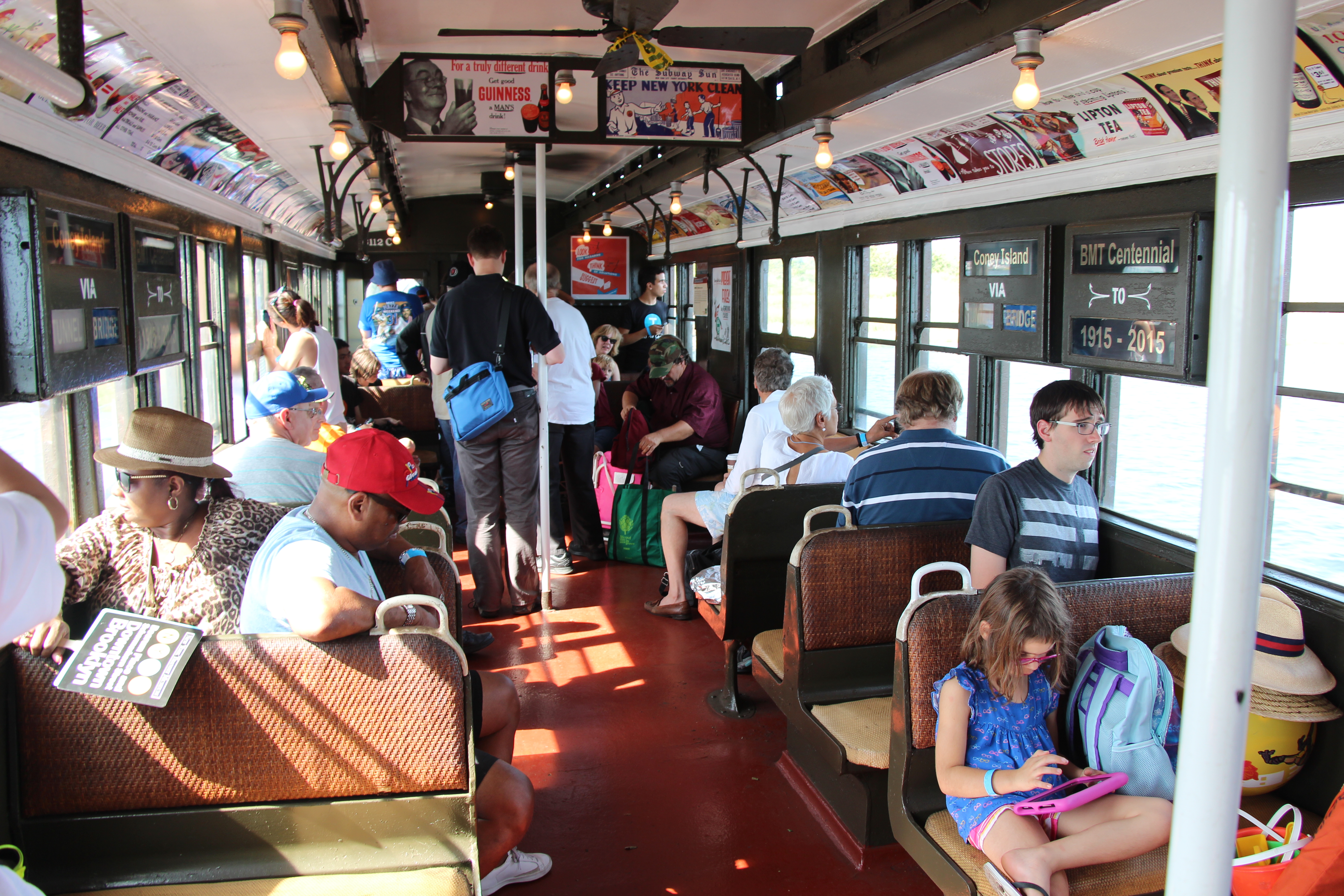 Riders onboard vintage train as it travels aboveground, sun streaming through windows.