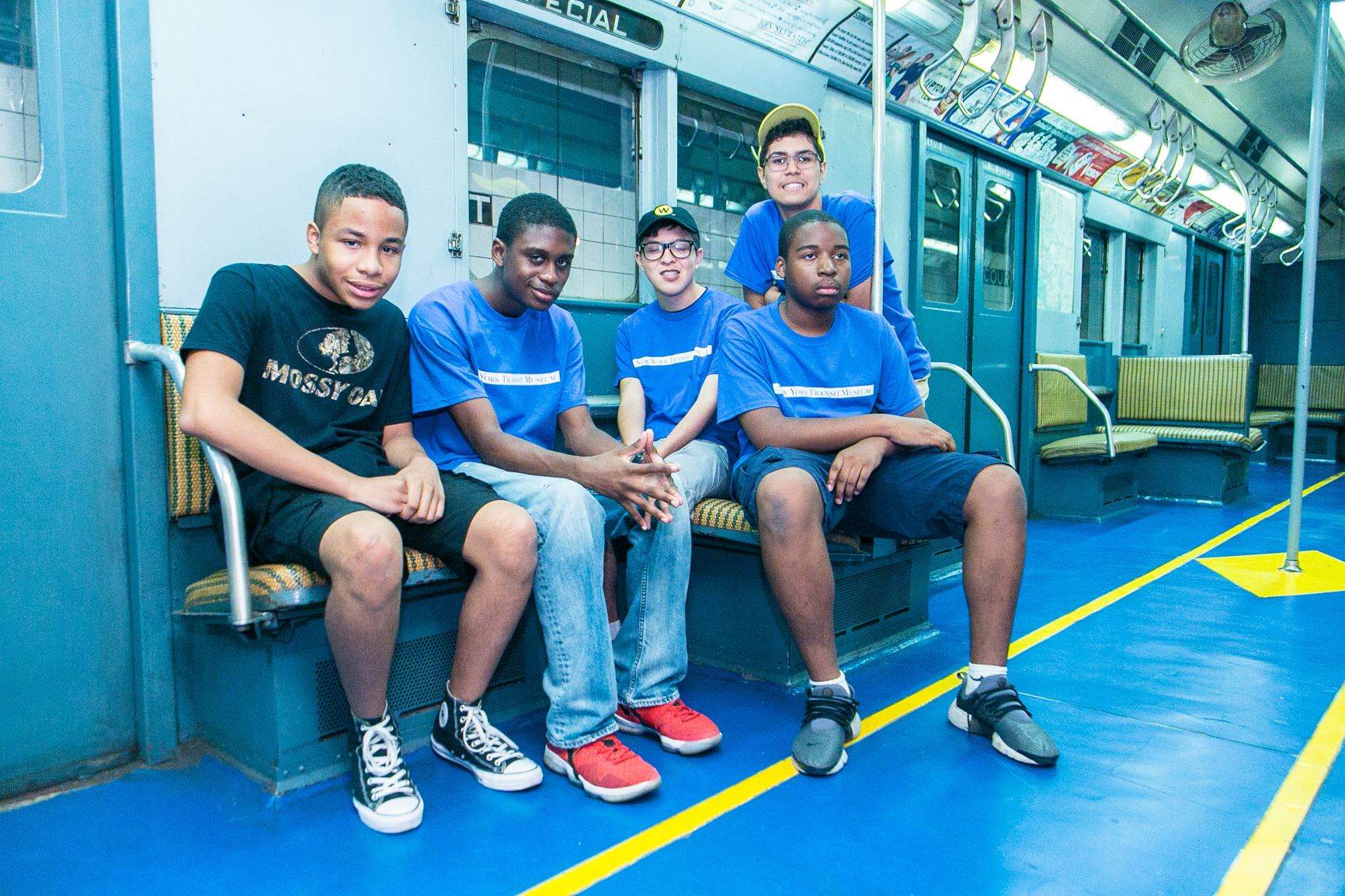 Five teens sitting on a subway car.