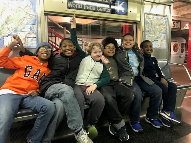 Six boys sitting and smiling together on a subway car.