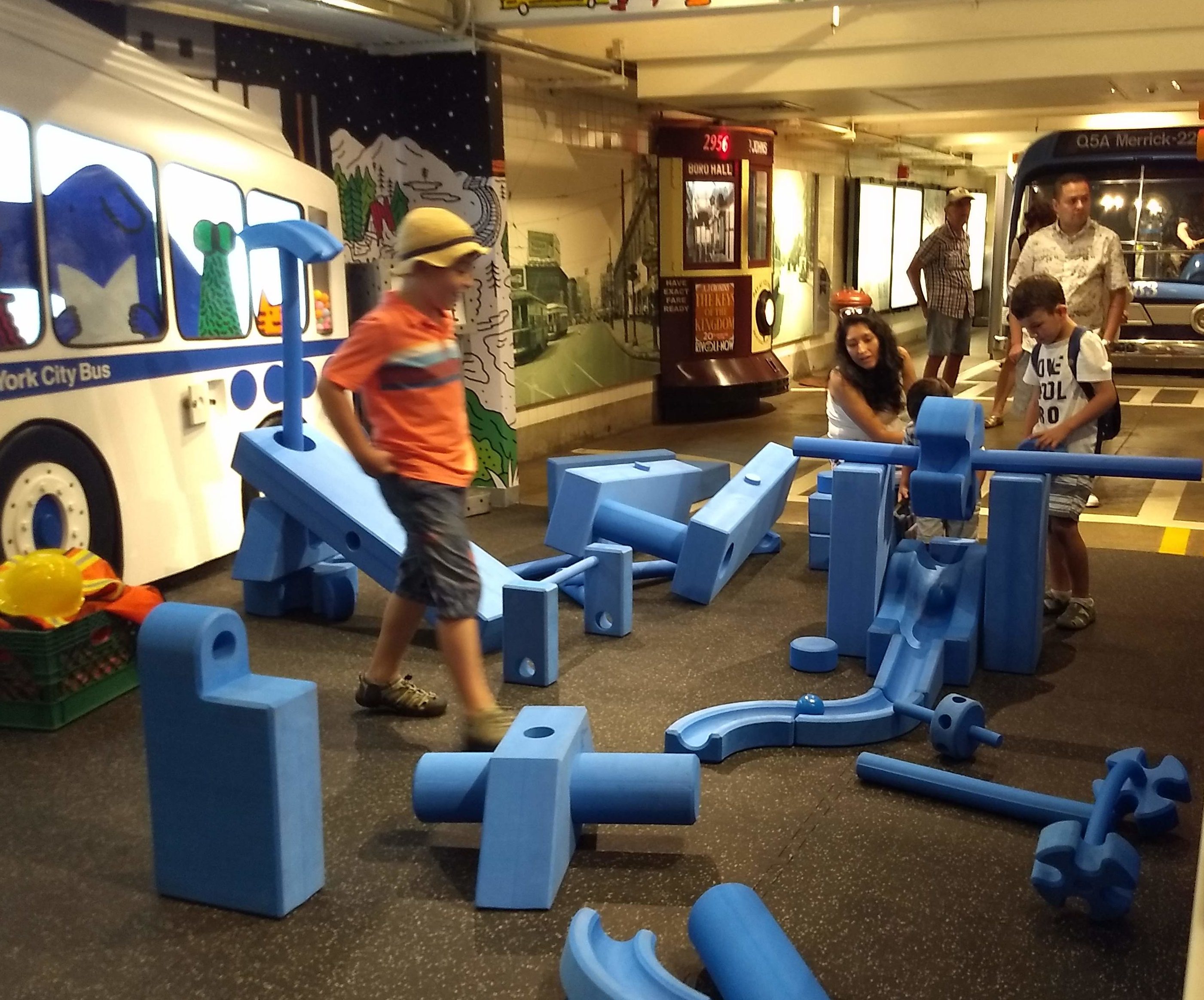 Children play with large blue blocks, building a large ramp for a ball together.