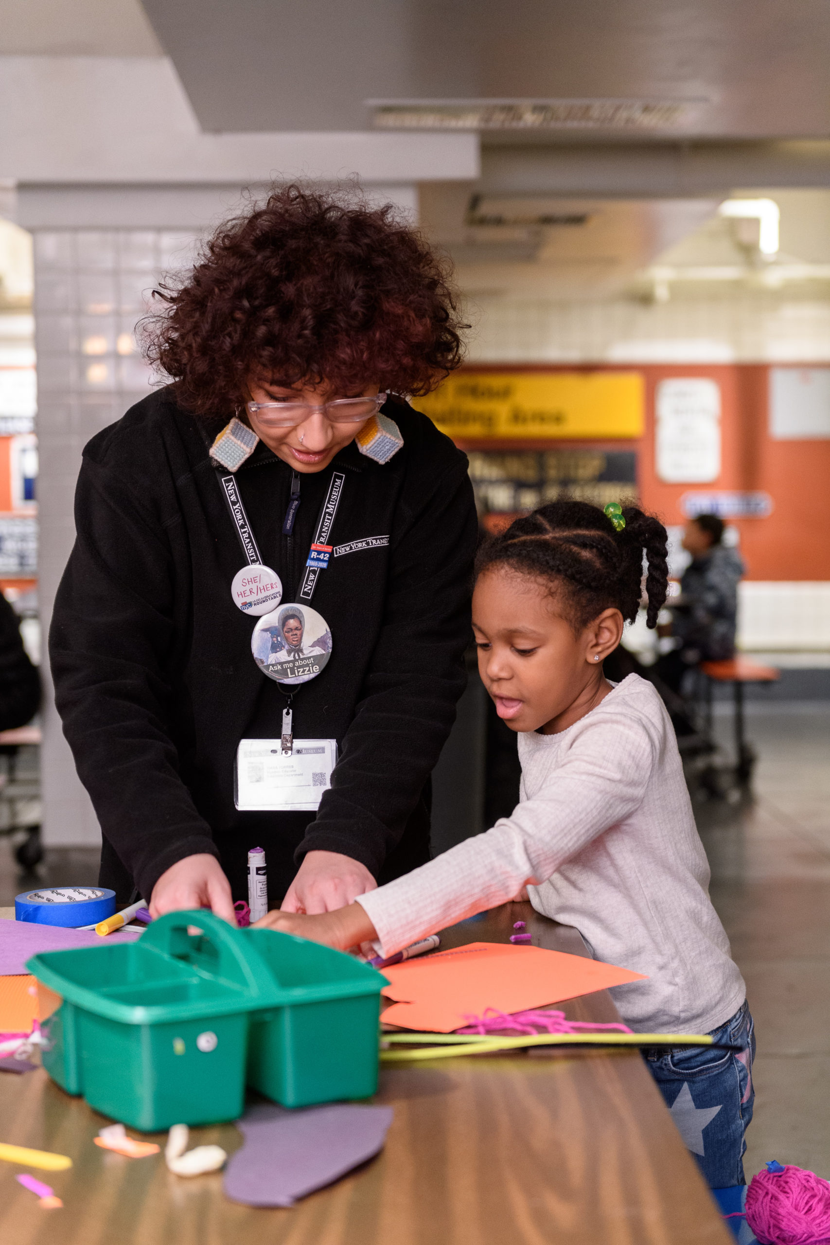 A museum educator and child stand at a table working on an art project.