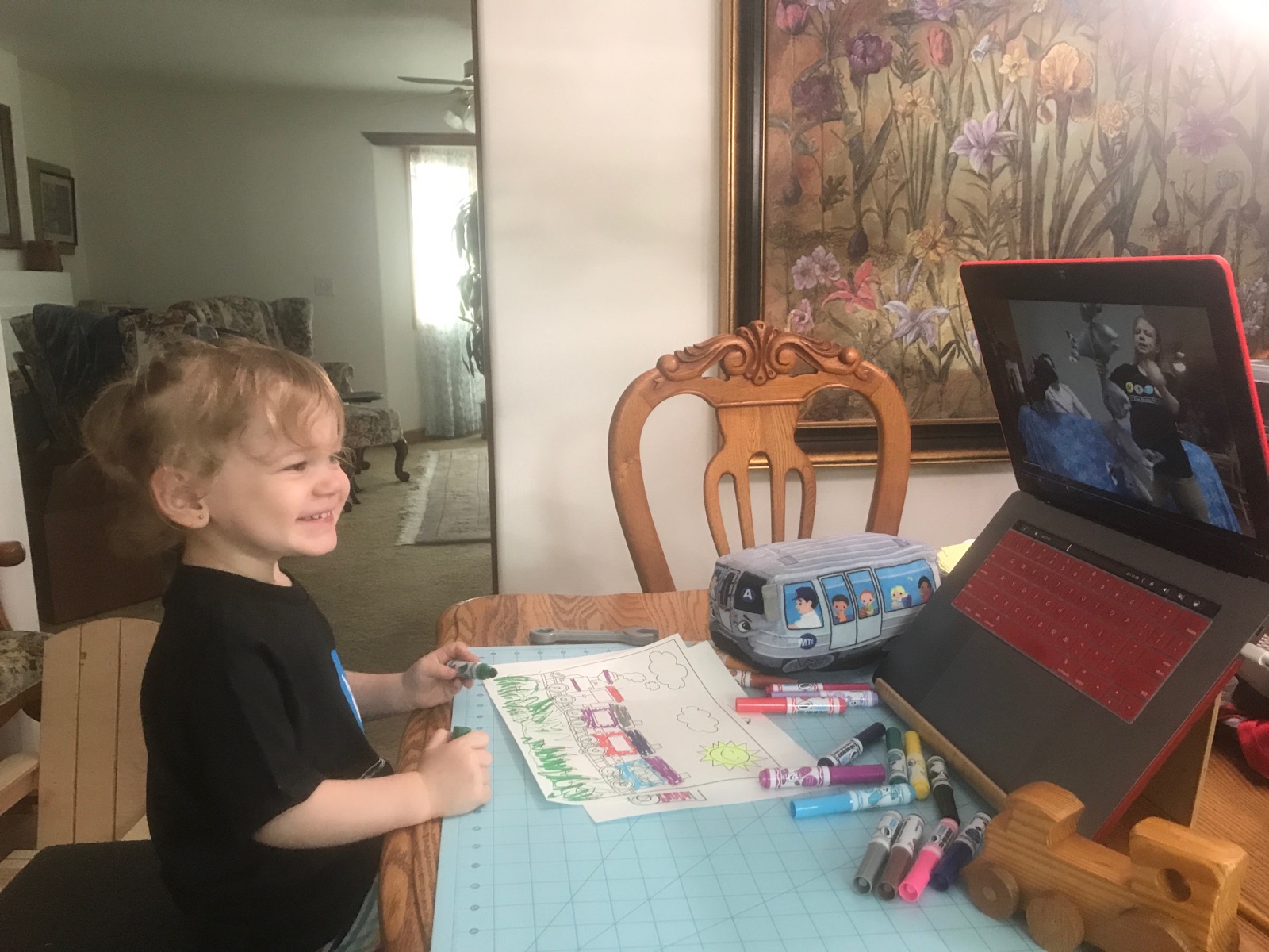 Child makes art at a table at home and smiles at a Museum educator on a computer screen.