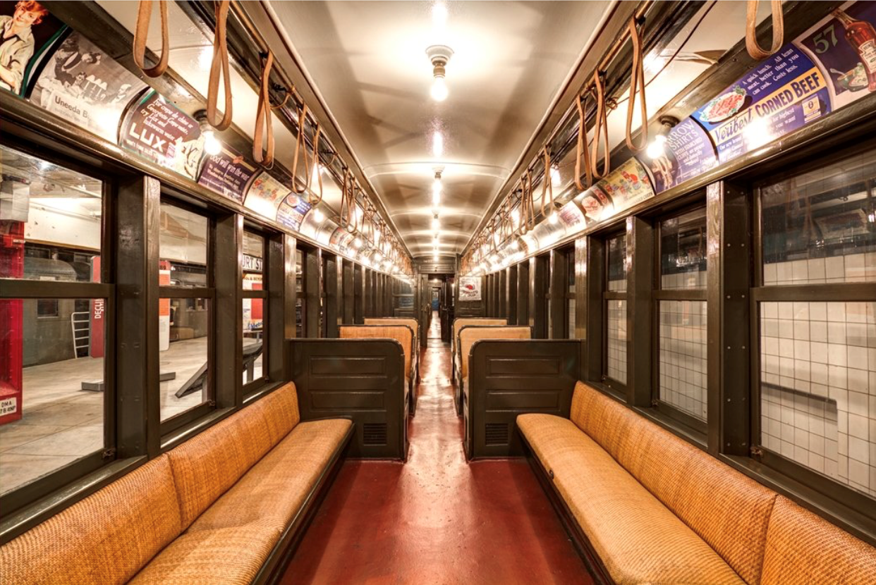 A view of the inside of a Brooklyn Union Elevated train car, with rattan bench seats and exposed light bulbs.
