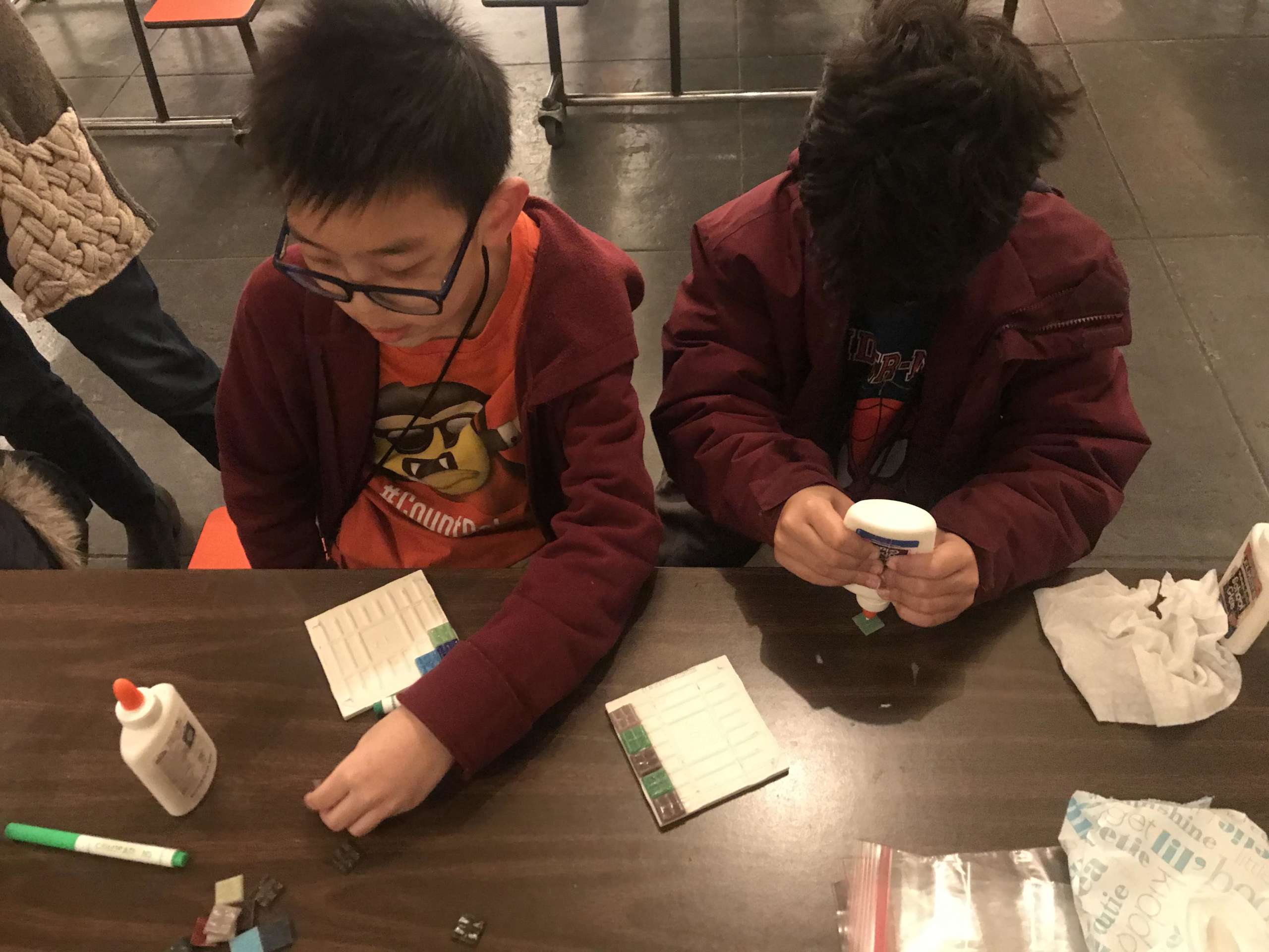 Two students glue together mosaics.