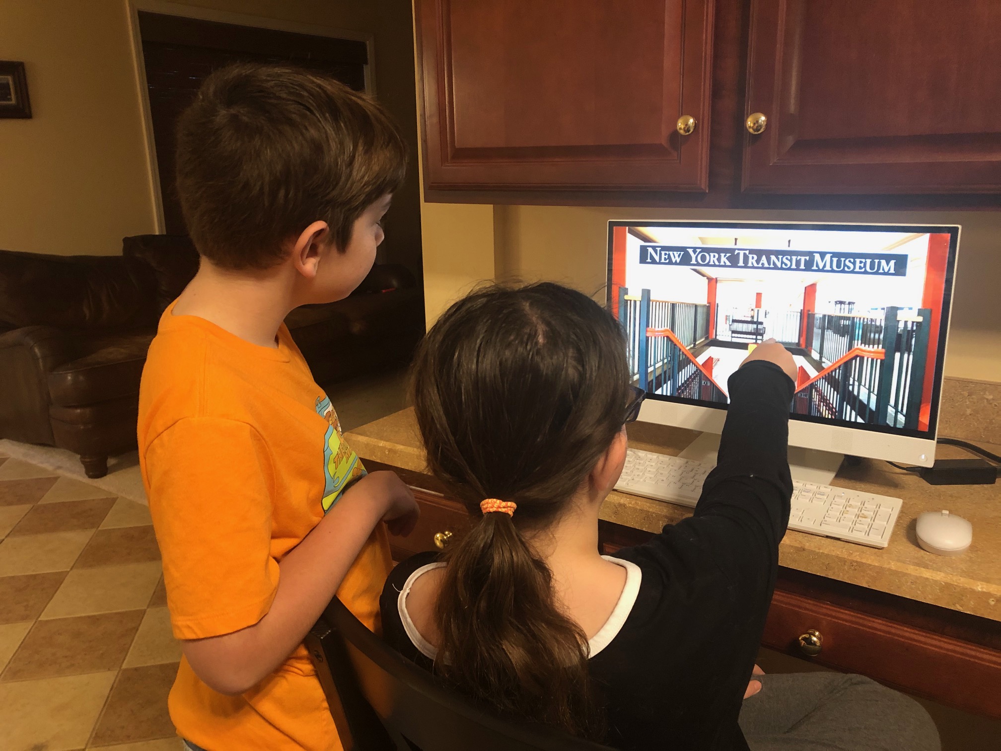 A brother and a sister engage with a virtual museum program on a computer.
