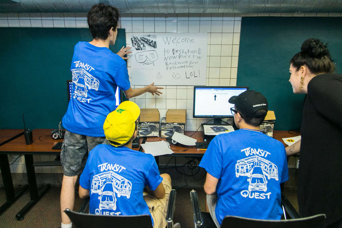 Three teens wearing Transit Quest tshirts and a museum educator in the computer lab.