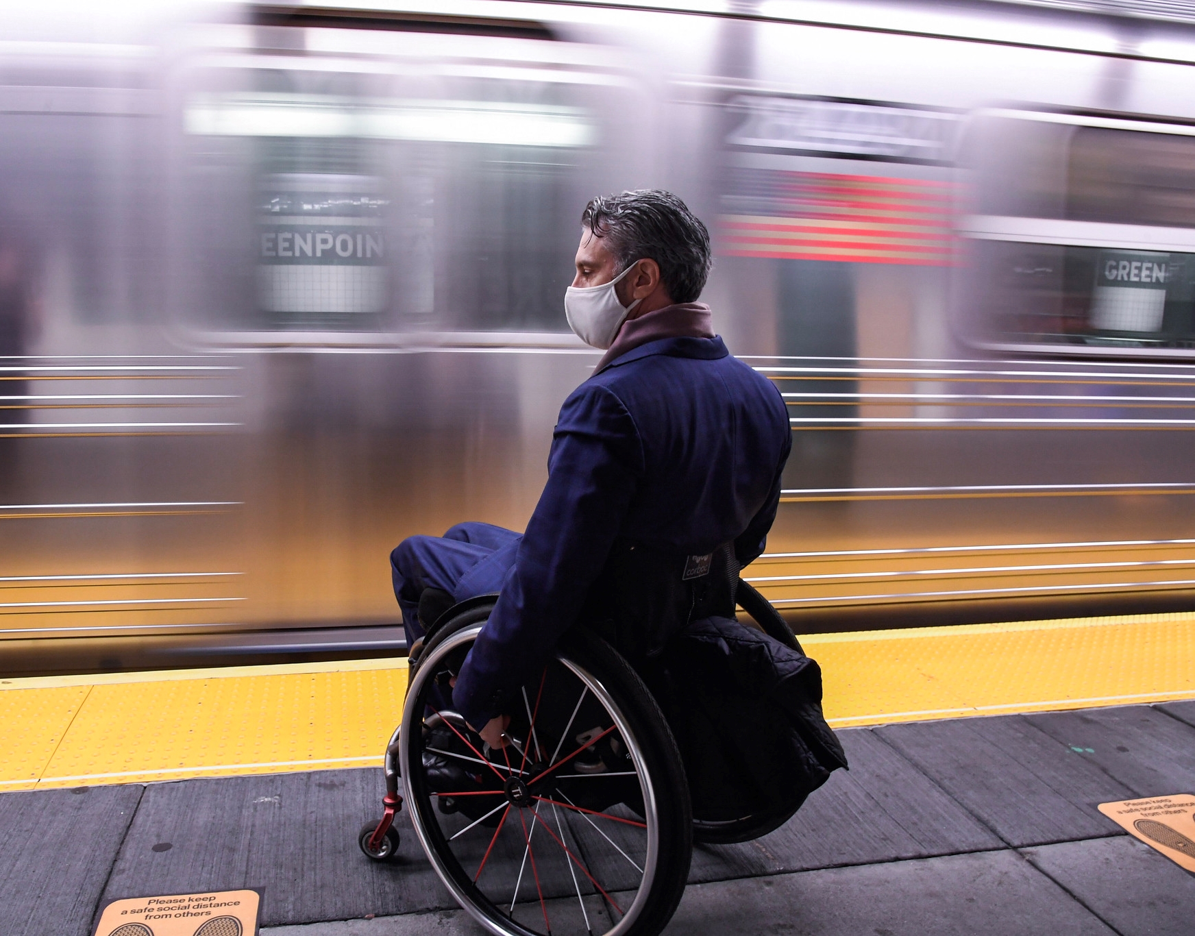 Man in wheelchair on subway platform in front of moving train