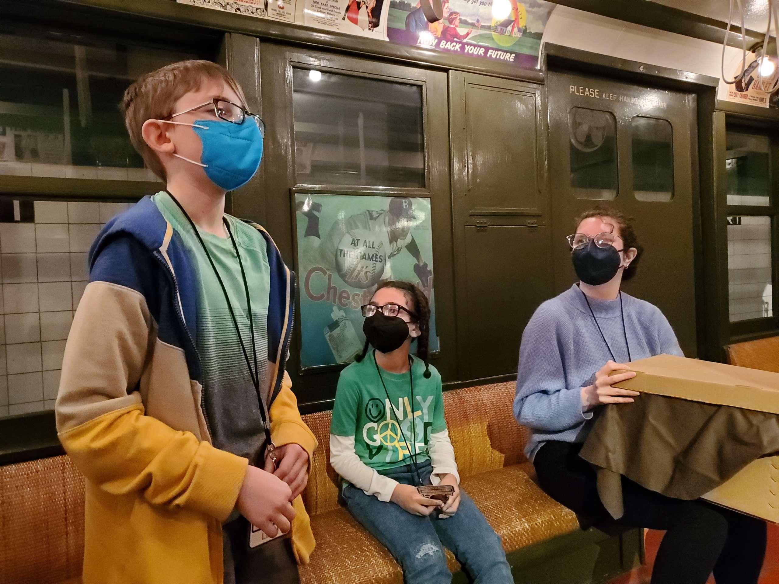 A student and a teacher sit on a vintage train car and look at another student standing with them.