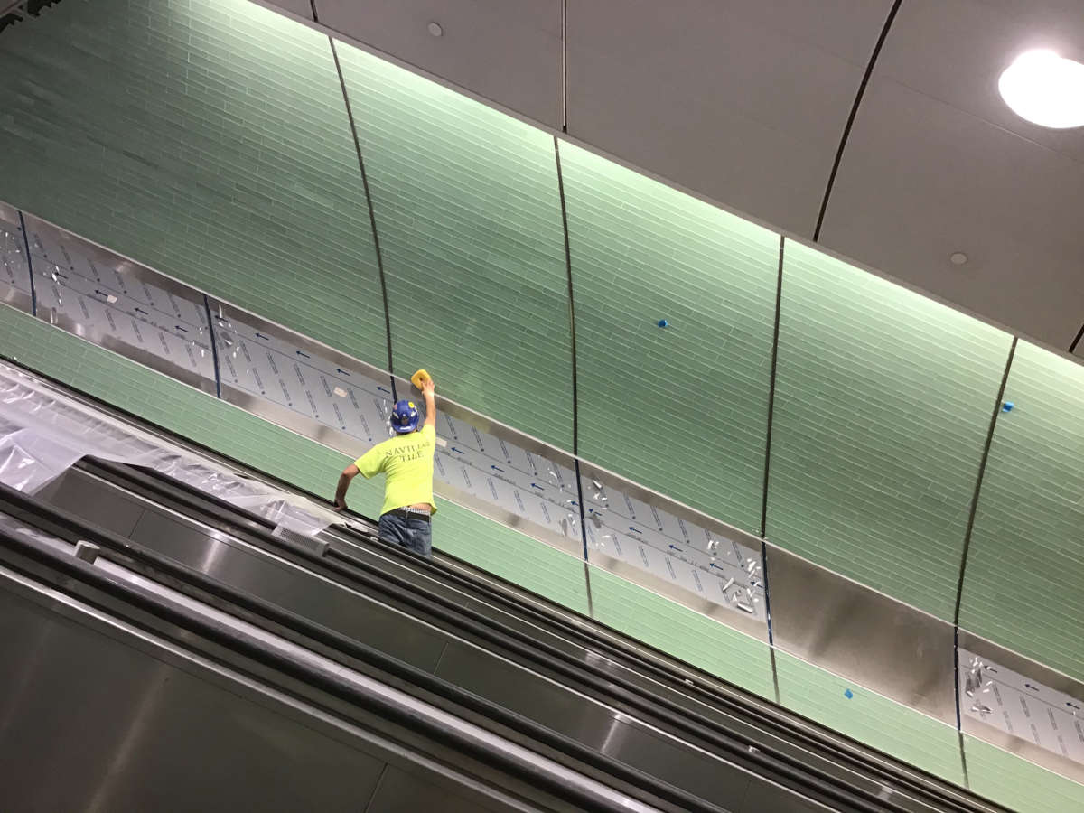 Applying grout to glass tiles in escalator wellway, 2020 