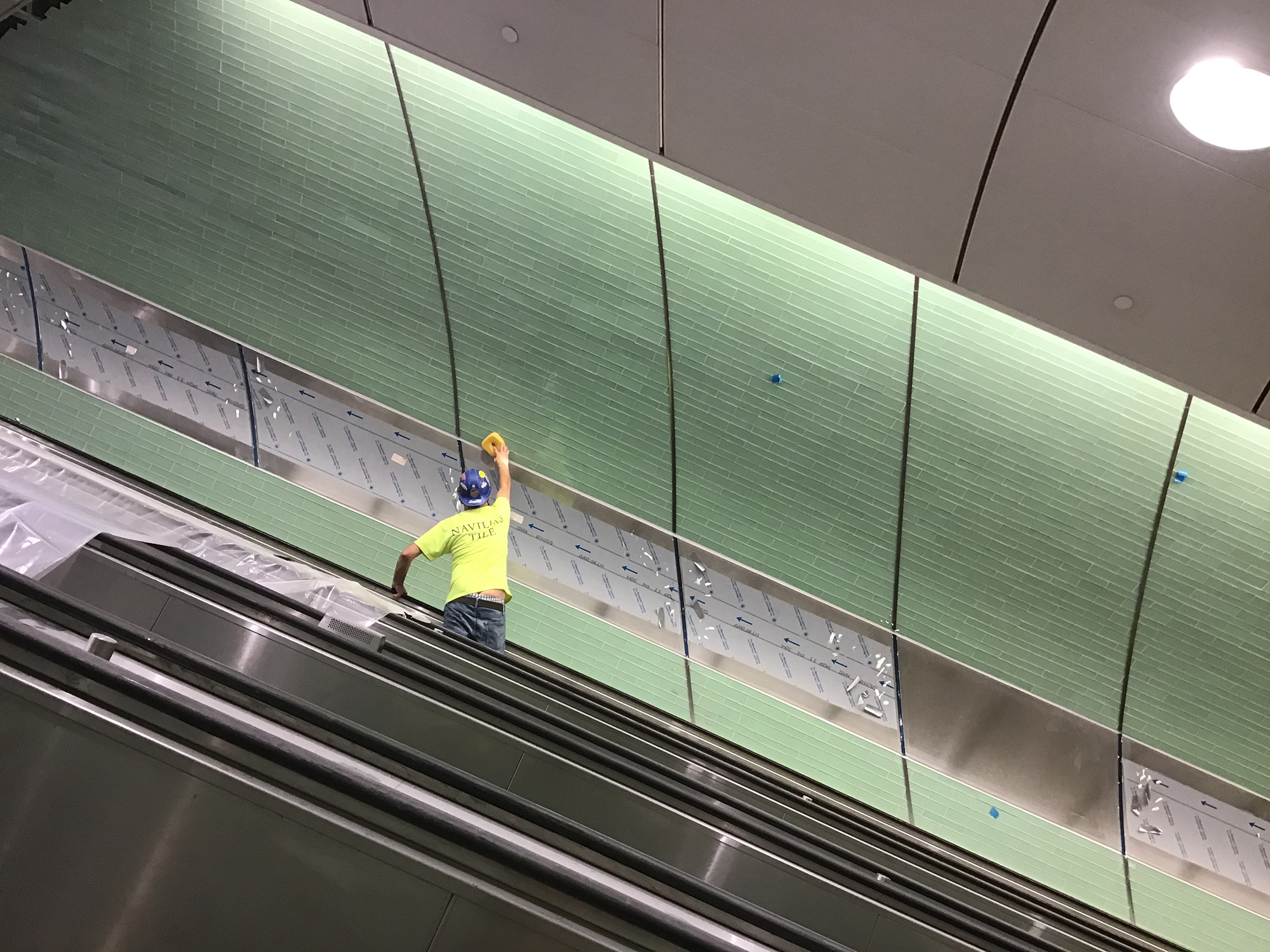 Applying grout to glass tiles in escalator wellway, 2020