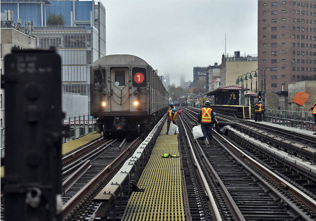 Color photograph of a 1 train on the tracks with construction workers.