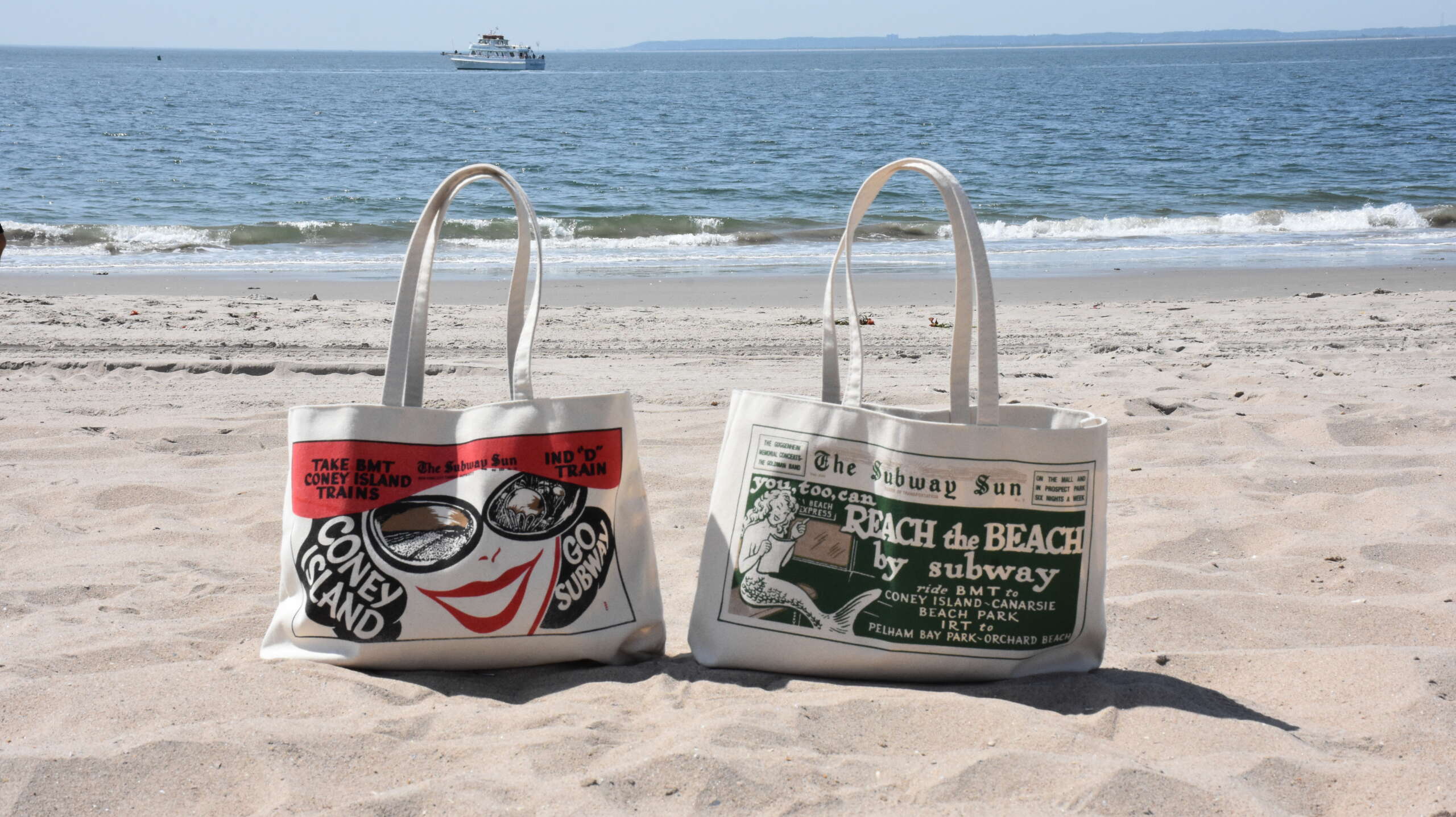 Two tote bags on the beach at Coney Island, both featuring artwork from vintage Subway Sun ads