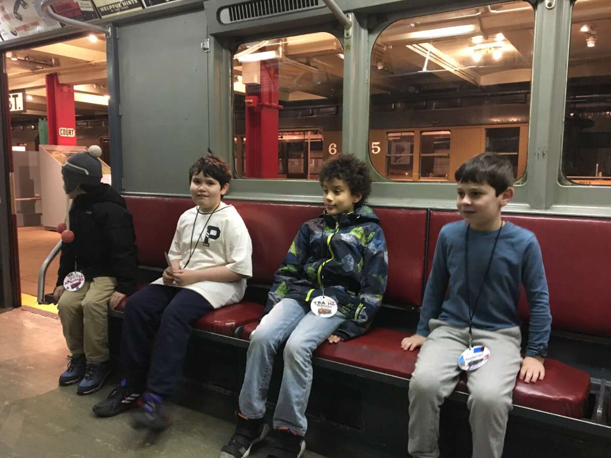 Four Subway Sleuths students sit on a vintage subway car.