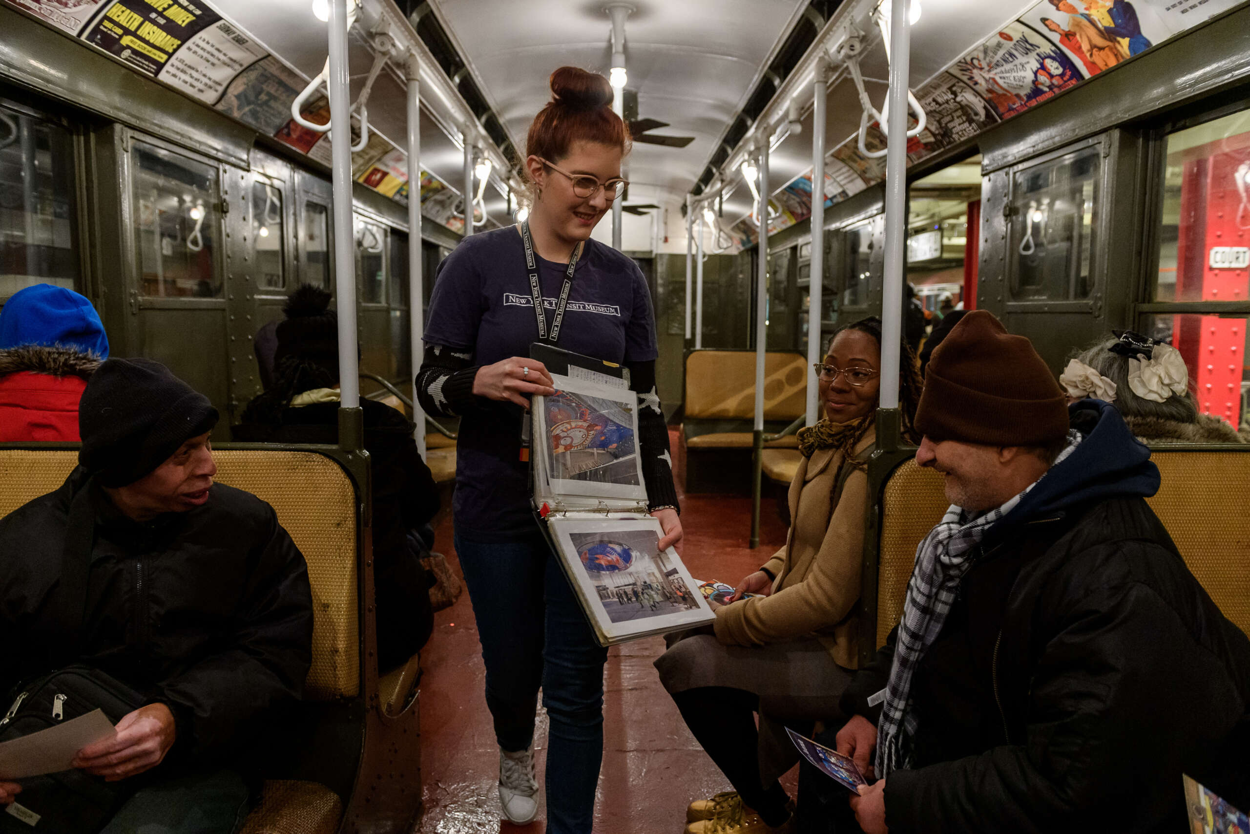 A Museum Educator shows images to visitors on a vintage subway car.