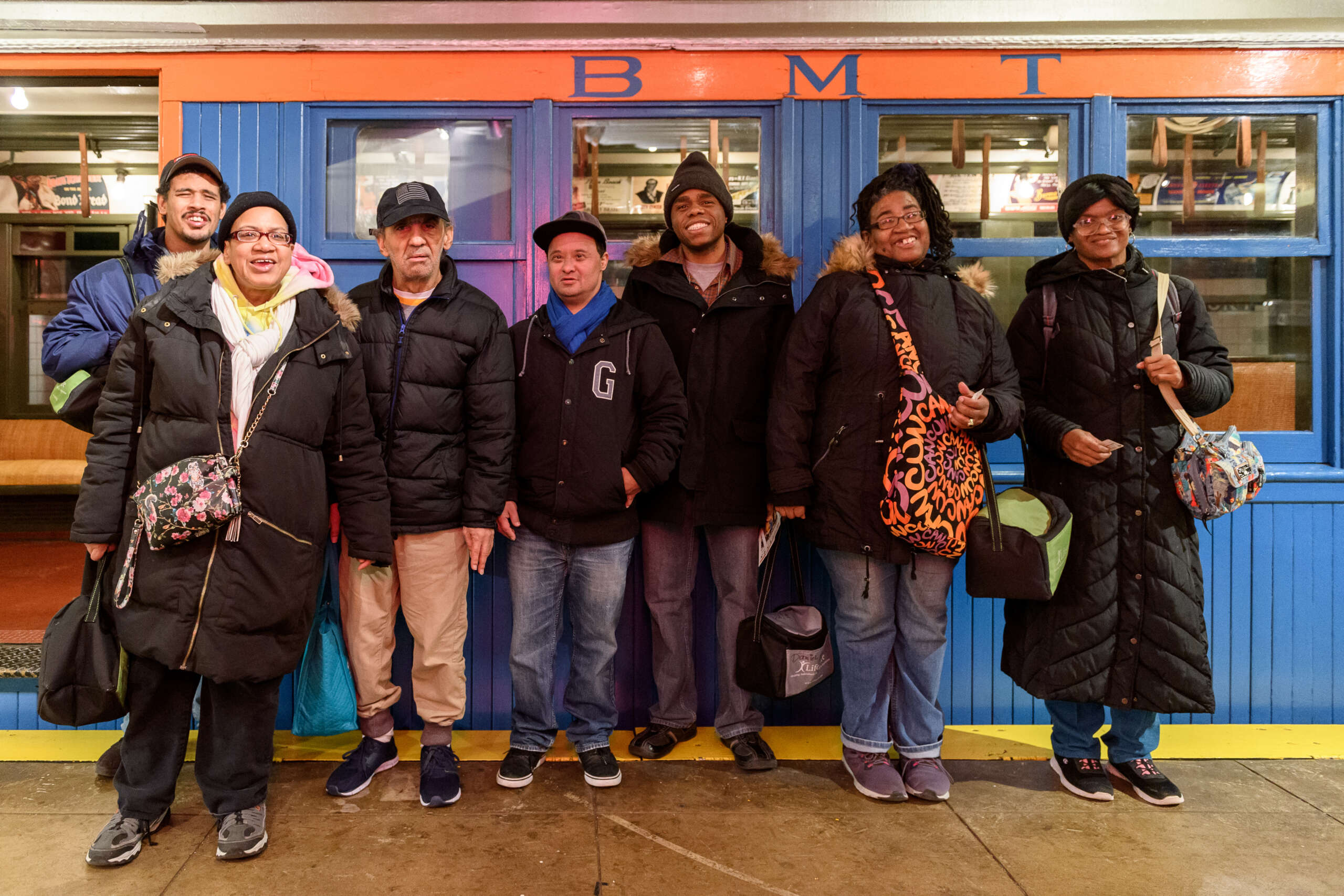 A group of adults stand in front of a blue and orange wooden train car.
