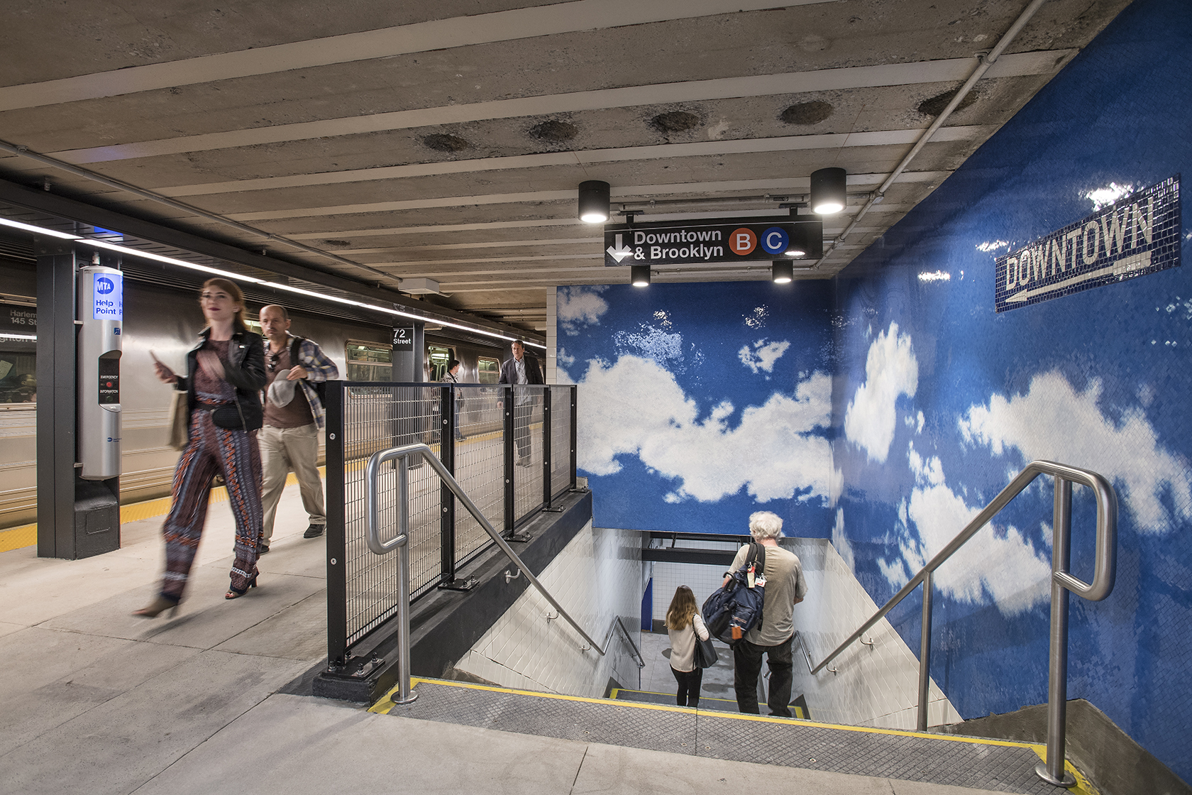 Commuters in a subway station walk by a mosiac of a blue sky and clouds next to a staircase.
