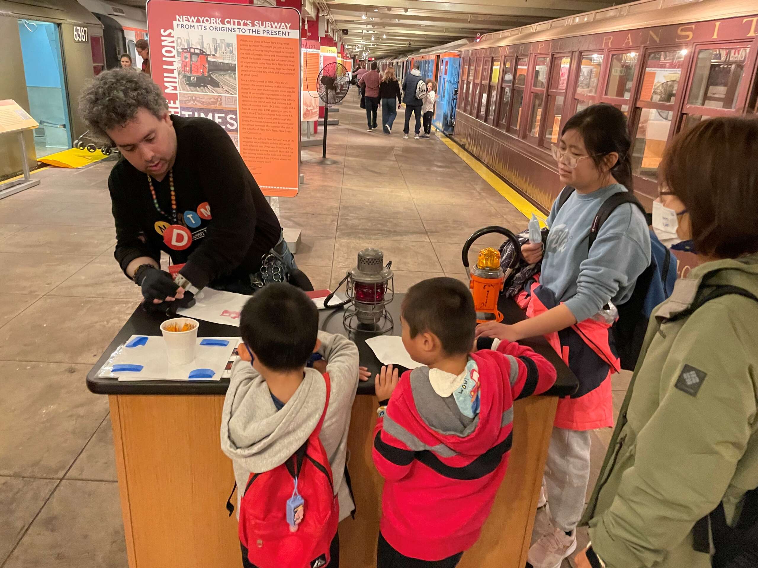 Museum staff engages with a family at the History on Wheels cart on the subway platform.