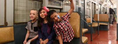 Three children with their face painted siting in a vintage subway car.