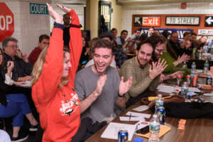 Woman raises arms to indicate success. Group at table applauds.