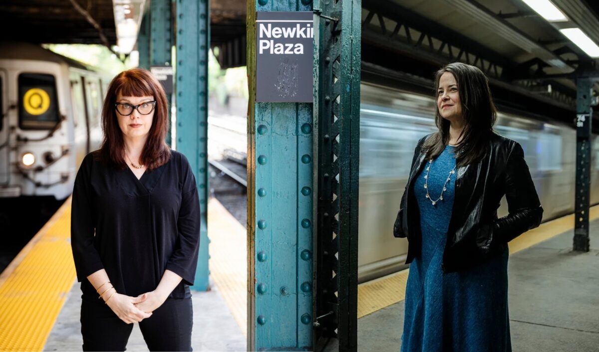 Two woman stand on a subway platform.