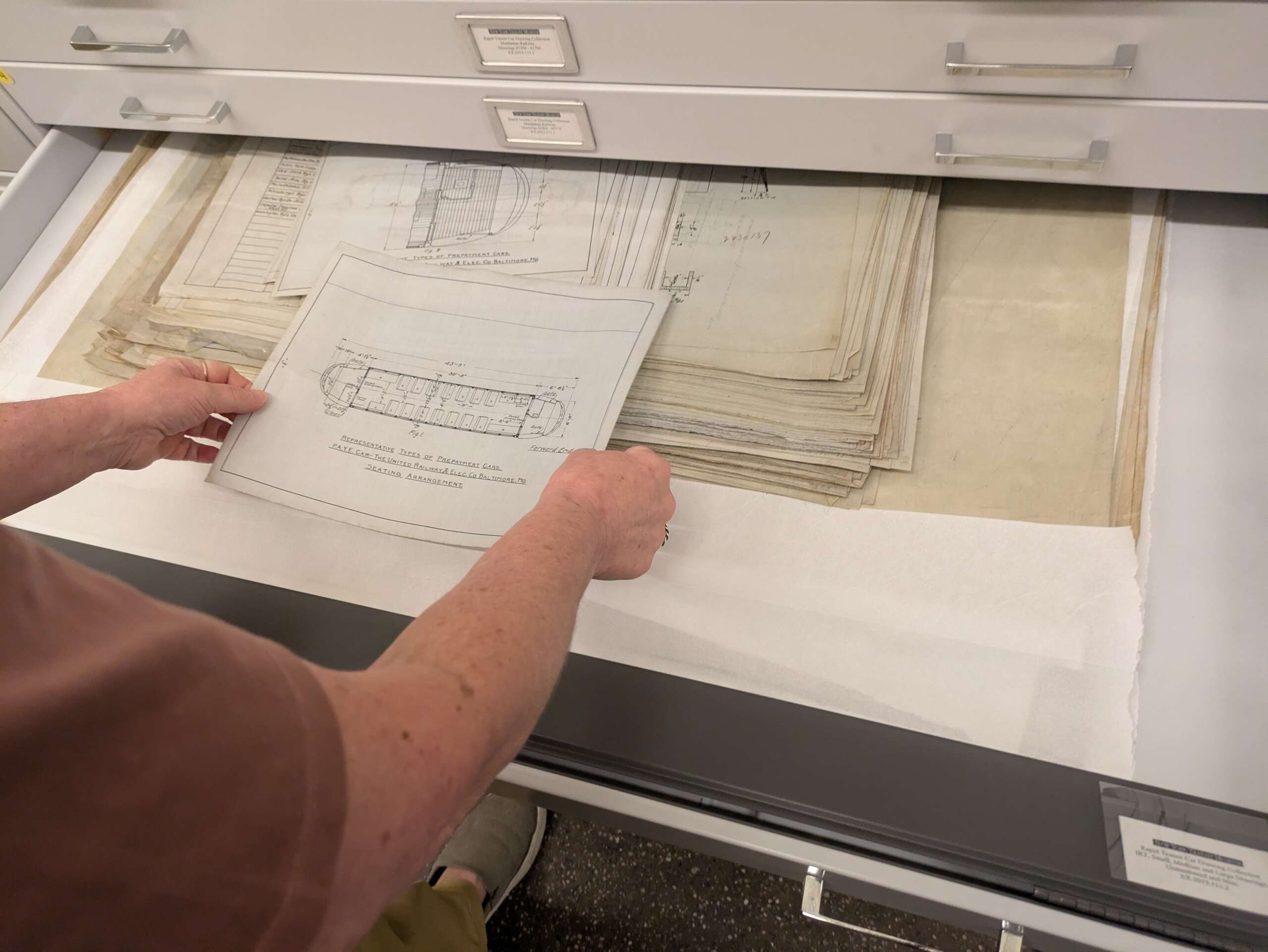 Hands pull design drawings out of an archive filing cabinet.