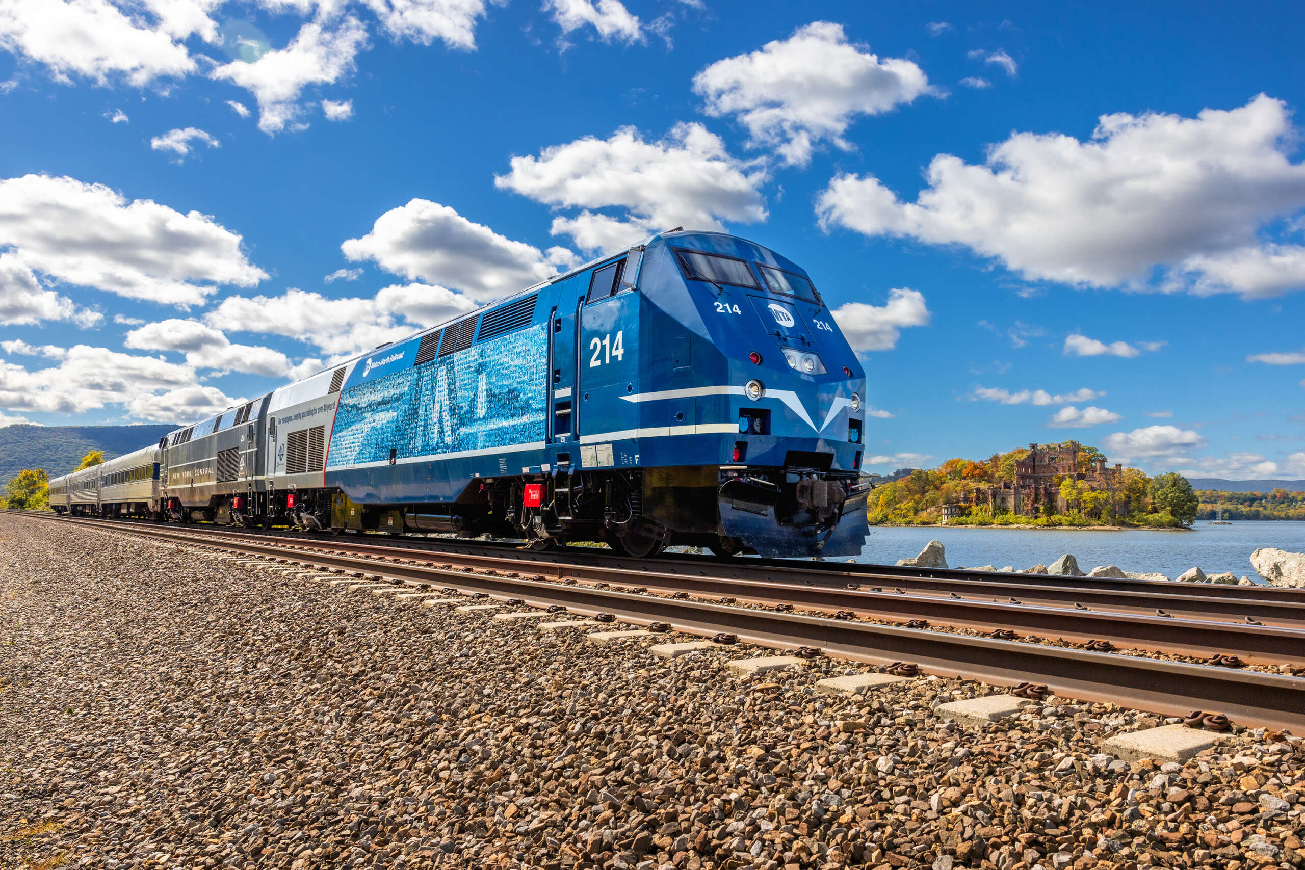 A train decorated to honor Metro North employees is posed on tracks with a castle in the background.