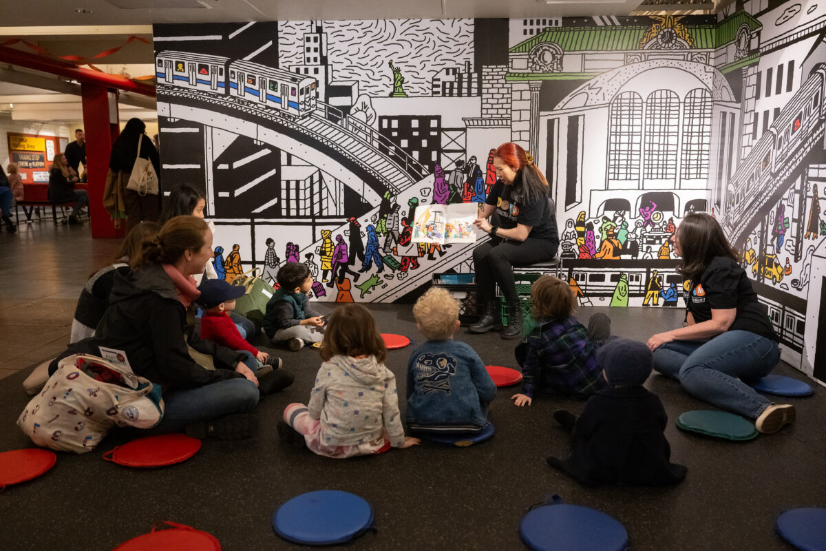 Museum staff member reads to group of babies, toddlers, and parents