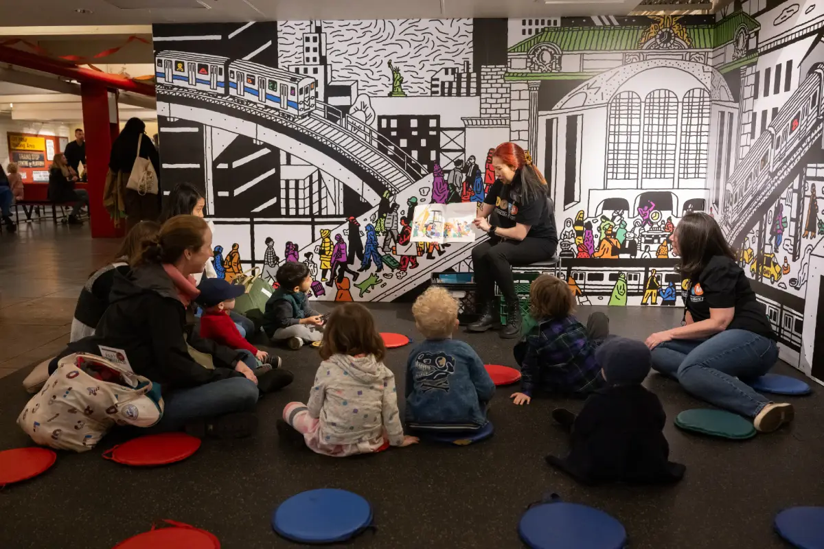 Museum staff member reads to group of babies, toddlers, and parents