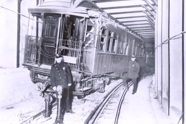 Man stands in front of wrecked wooden train in tunnel below Malbone Street