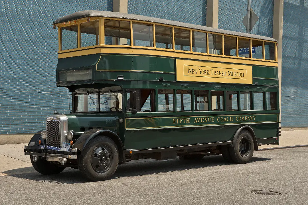 A vintage yellow and green double decker bus, one of the oldest buses in the New York Transit Museum's fleet.