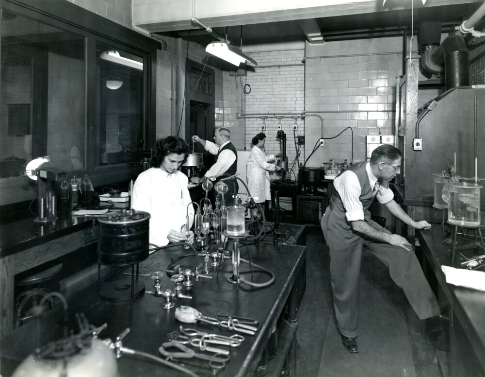 Scientists work on equipment on various tables in a laboratory.