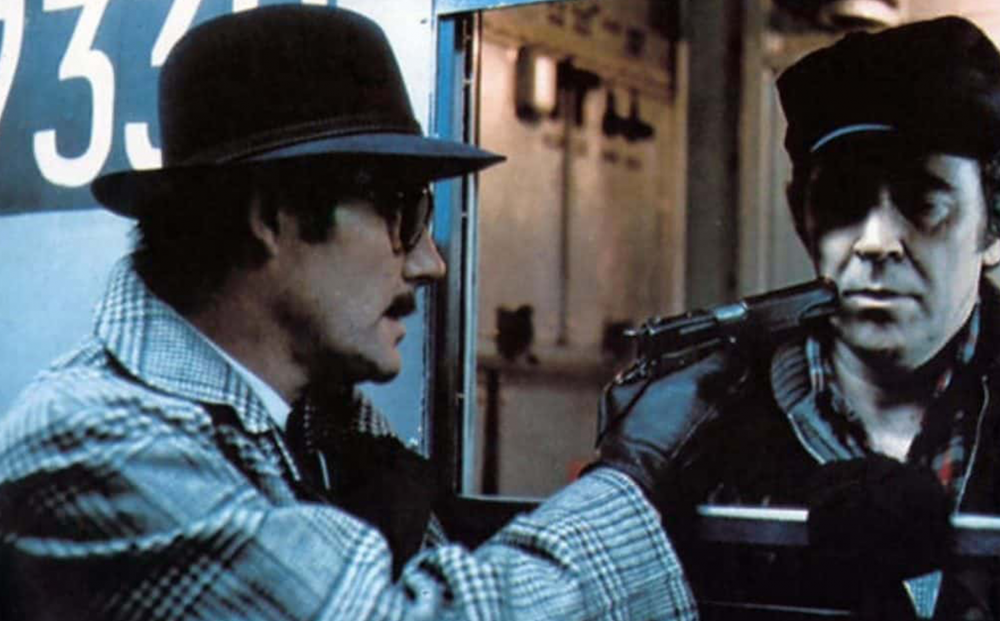 A man in a hat points a gun at another man.