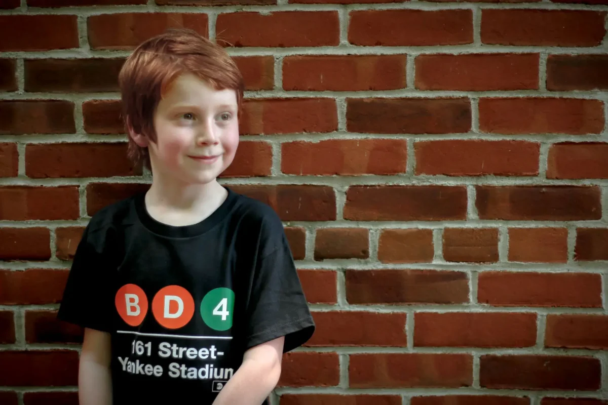 Young boy in Yankees subway t-shirt in front of brick wall